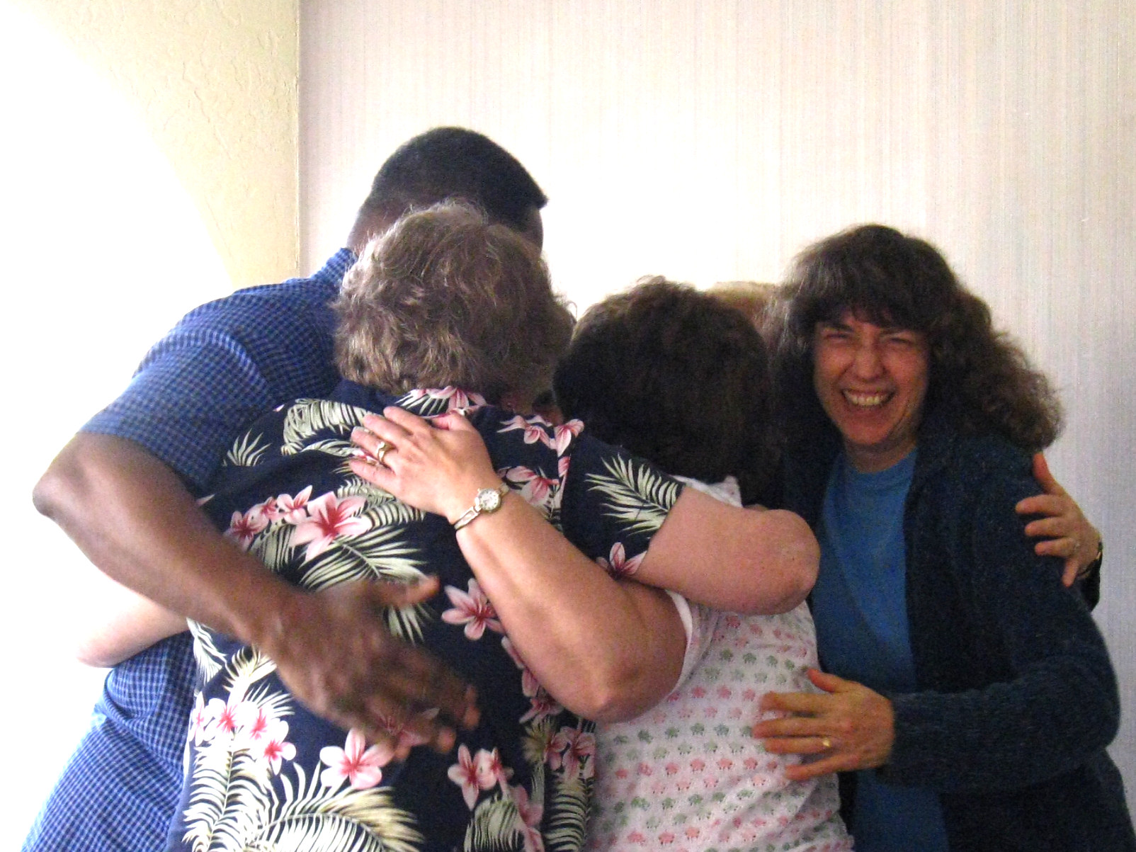 4 people in a group hug. All are facing inward, one facing the camera with a huge smile