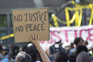 800px-A_demonstrator_holds_a_No_Justice_No_Peace_sign_at_the_rally_for_Philando_Castile_outside_the_Governor's_residence_in_St_Paul_MN_7-7-2016_(28137456646)