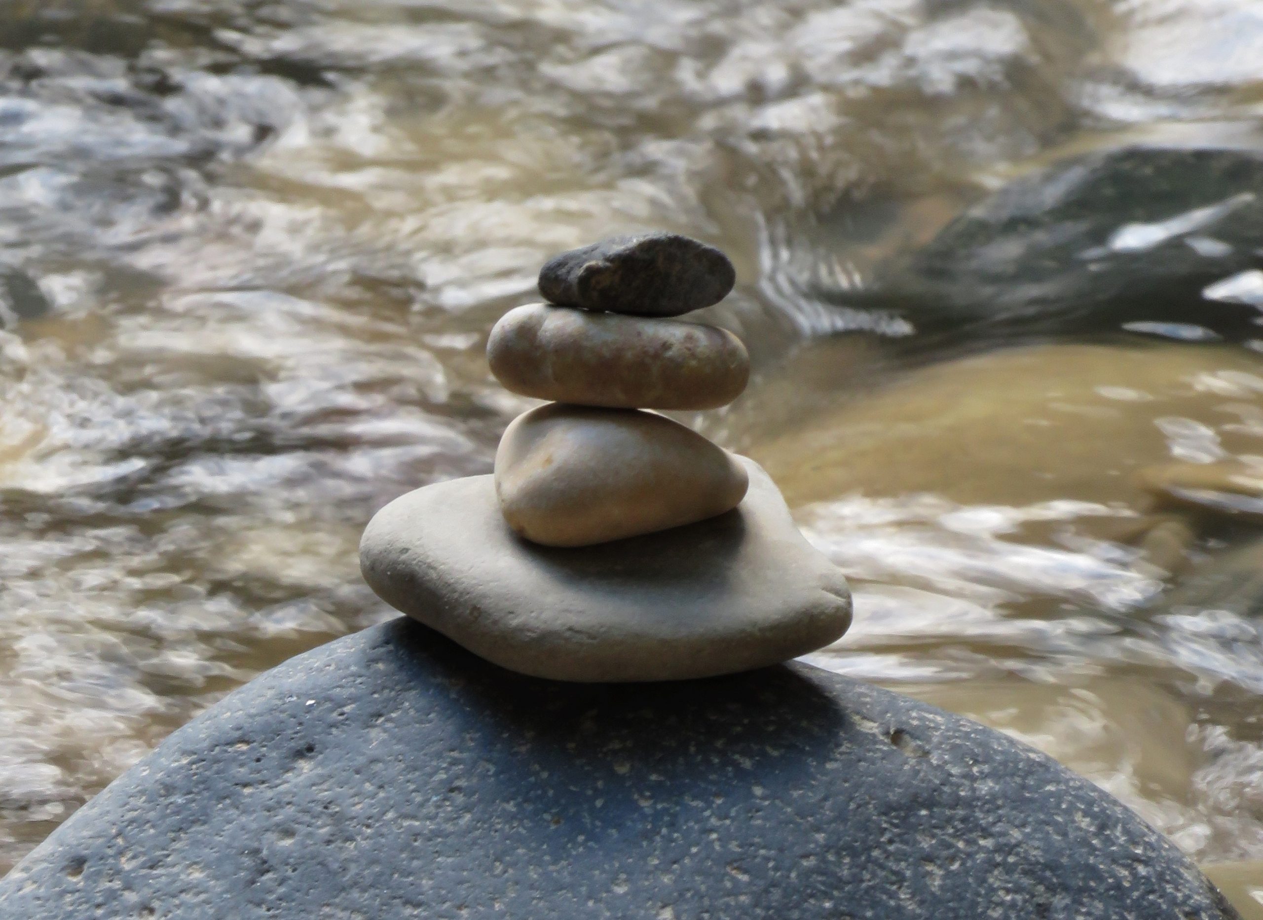 A cairn (stack of stones) sitting in front of a running river. Cairn is steady, river is flowing.