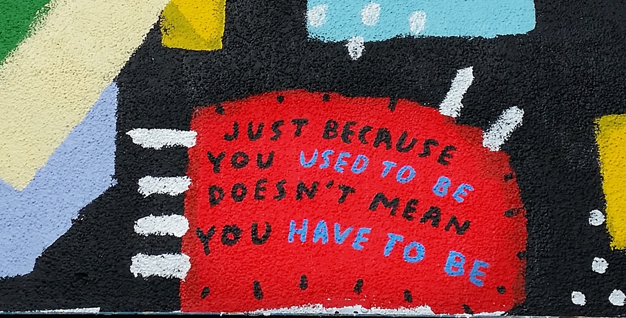 Portion of a mural comprised of bright colored splotches that look like a child drew them. The center splotch contains the words "Just because you used to be doesn't mean you have to be."
