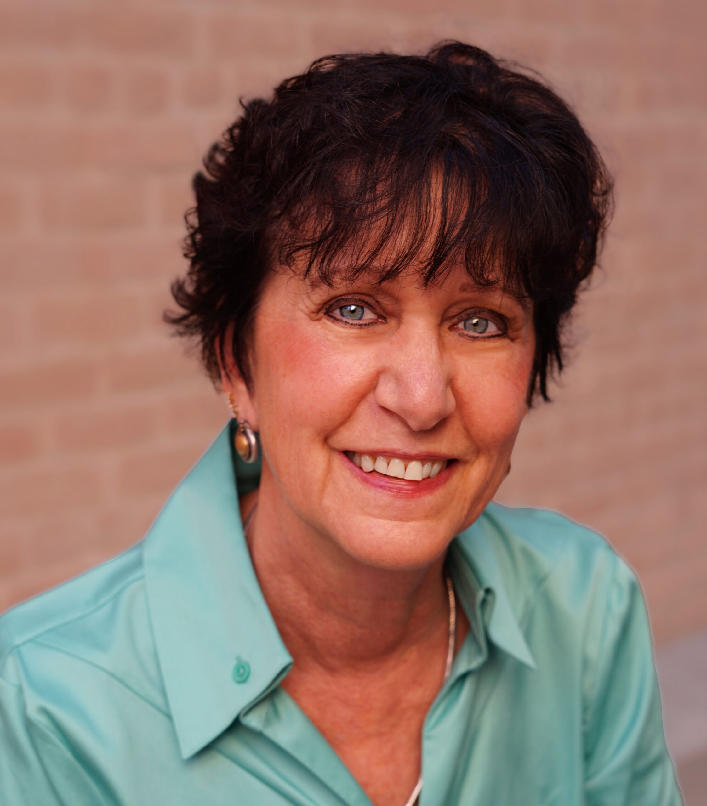 Photo of Hildy, dark hair, blue eyes, turquoise blouse, against the background of a brick wall