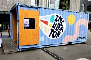 Corrugated shipping container painted light blue with the word INCUBATOR painted on the side