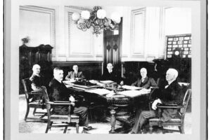 1880's era B&W photo of a group of old white men in formal business attire, sitting around a board table